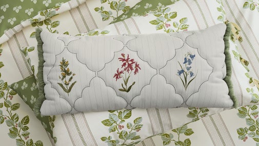A pillow with a scallop pattern and flowers sits on patterned bed lining